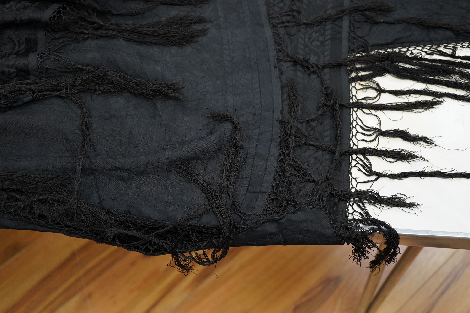 A Edwardian black silk damask paisley patterned shawl. Possibly a mourning shawl.178cm x 156cm. Condition - one small hole, otherwise good.